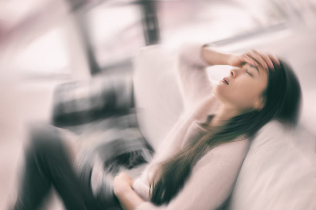 Sick woman with headache feeling faint vertigo holding head in pain with fever and migraine. Blurry motion blur background Sick woman with headache feeling faint vertigo holding head in pain with fever and migraine. Blurry motion blur background.